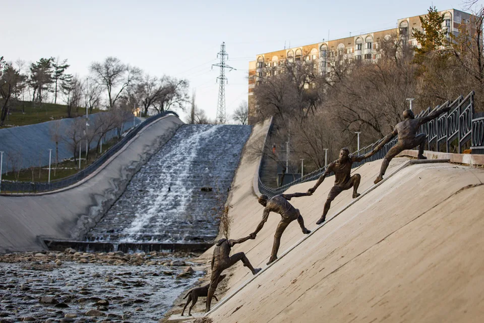 Bronze figures linking hands down a reservoir bank to reach a dog